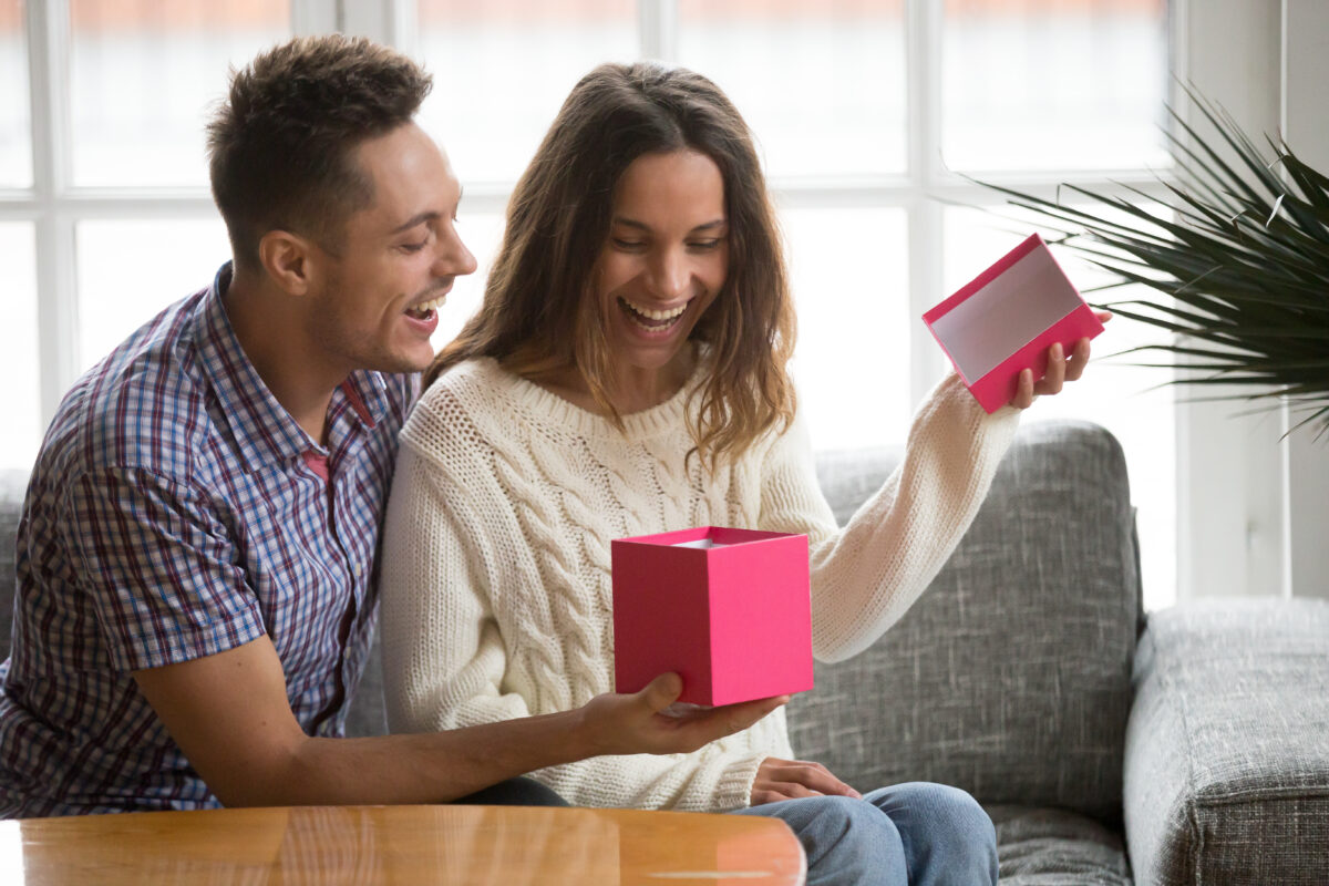 Nadšená mladá žena otevírá dárkovou krabičku a dostává dárek od manžela